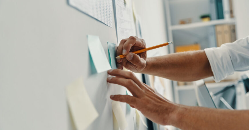 Close up of man writing something using adhesive notes while working in the office